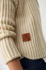 Sweater de punto grueso en color crudo, con cuello alto y diseño de canalé vertical. Presenta mangas largas con corte raglán y un ajuste holgado.