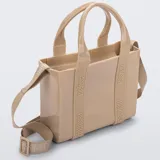 Cartera tipo tote bag Melissa modelo Mini Dulce, color beige con acabado brillante. Está fabricada en Melflex, un material de PVC flexible, e incluye asas de mano fijas y una correa ajustable y extraíble de tela con el nombre de la marca grabado.