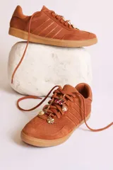 Zapatillas bajas color marrón con cordones y charms dorados.