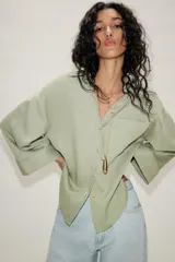 Camisa oversize color verde menta, con cuello camisero, cierre frontal de botones, bolsillo de parche en el pecho y mangas anchas por debajo del codo.