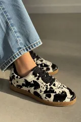 Championes de cuero vacuno con estampado animal print tipo vaca en blanco y negro, cordones negros y suela de goma color caramelo.