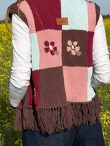 Chaleco tejido de punto con diseño de bloques de colores en tonos marrón, bordó, rosado y celeste, con detalles florales bordados y flecos en el ruedo.