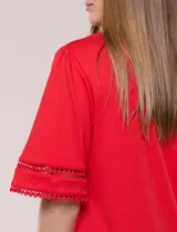 Remera blanca de silueta recta y algodón suave, con escote redondo y pequeña abertura central tipo gota. Presenta mangas de largo intermedio con aplicación horizontal de puntilla calada al tono y ruedo recto con tajos laterales.