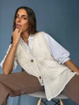 Chaleco tejido color tostado con destellos de lurex, escote en V y cierre frontal con botones. Presenta detalles de bordados y terminaciones en crochet en color crudo.