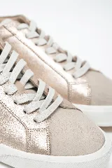 Championes Selen color dorado con acabado metalizado, confeccionados en cuero legítimo. Presentan cordones blancos, suela de goma blanca y detalles en gamuza beige en el talón.