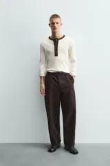 Camiseta de manga larga en tejido de punto canalé color crudo, con cuello redondo y tapeta frontal con botones en color marrón oscuro a contraste.