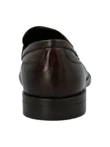 Mocasín estilo penny loafer para hombre, confeccionado en cuero marrón oscuro con textura sutil, punta redonda y suela plana con pequeño tacón.