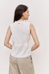 Blusa sin mangas de color blanco, con cuello redondo fruncido y cierre frontal de botones. Combina un cuerpo texturizado con una parte inferior de encaje calado y diseño peplum.