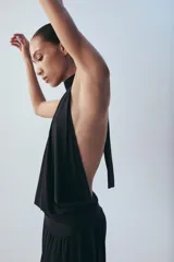 Mono largo negro con cuello halter, hombros descubiertos, parte superior drapeada y piernas anchas con bajo acabado en puño elástico.