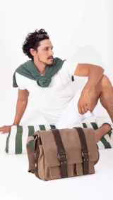 Morral de tela canvas color marrón claro con detalles en cuero sintético marrón oscuro. Tiene tapa frontal con dos correas ajustables, múltiples compartimentos y correa de hombro ajustable.