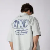 Camisa de manga corta color marfil, corte boxy, con cuello camisero, cierre frontal de botones y pequeño bordado marrón en el pecho con las siglas VCP.
