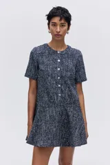 Vestido corto de tejido bouclé en tonos azul marino y blanco, con cuello redondo, manga corta y cierre frontal con botones metálicos decorativos. La falda tiene un corte acampanado con vuelo.