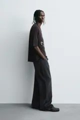 Camiseta negra de algodón con corte boxy fit y cuello redondo. Presenta un estampado gráfico desgastado con temática espacial o celestial en tonos azules y blancos, y texto en la parte superior e inferior.