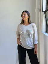 Remera de manga larga color beige con diseño frontal de parches decorativos con lentejuelas plateadas y encaje.