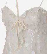 Blusa corta color crema con escote corazón, confeccionada en tejido con textura de lunares y volados de chifón. Presenta breteles finos ajustables y un lazo decorativo en el centro del busto.