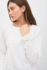 Remera de manga larga color blanco, confeccionada en tejido suave con textura acanalada. Presenta volados verticales decorativos en el frente y en los puños, con un calce cómodo y favorecedor.