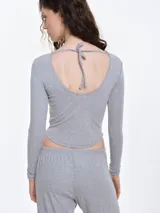 Remera de manga larga entallada confeccionada en tejido pointelle suave, con escote a la base y detalle de pequeño lazo decorativo en el centro. Presenta terminaciones con borde picot.