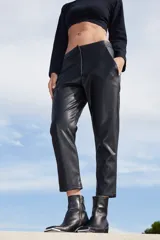 Pantalón sastrero de ecocuero negro, con corte recto, bolsillos delanteros y traseros, y botamanga irregular más corta en la parte frontal.