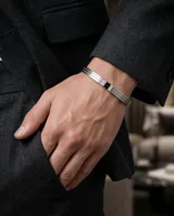 Esclava rígida de acero inoxidable con diseño de tres bandas paralelas y detalle central con piedra de circonia negra flanqueada por pequeñas incrustaciones brillantes.