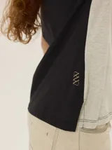 Remera de manga corta con diseño colorblock en tonos blanco, negro y beige, escote redondo y costuras verticales decorativas en el centro.