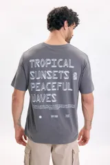 Remera gris oscuro de manga corta, con estampa tipográfica grande en la espalda con el texto 'Tropical Sunsets & Peaceful Waves'.