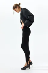 Leggings negros de tiro alto en punto elástico, con pliegues frontales pespunteados y estribos en los tobillos.
