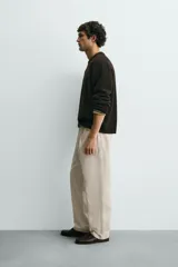Pantalón relaxed fit color beige confeccionado en tejido de algodón con tacto suave, cintura con pliegues delanteros y cierre frontal con cremallera y botón.