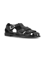 Sandalias de cuero color negro, de estilo romano con tiras cruzadas en el empeine, hebilla metálica de ajuste lateral y suela plana.