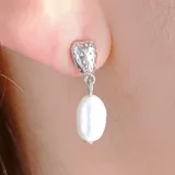 Aros colgantes dorados con base texturizada y una perla ovalada.