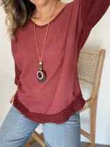 Remera blanca de manga larga con cuello redondo y detalle de tejido crochet en el dobladillo. Incluye un collar fino dorado como accesorio.