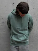 Canguro con capucha de color verde, con bolsillo frontal tipo canguro, cordones ajustables y pequeño logo bordado en el pecho.