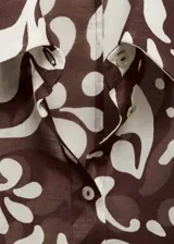 Camisa de algodón con estampado abstracto de hojas en tonos marrón y beige. Presenta cuello camisero, cierre frontal con botones y mangas largas con puños abotonados.