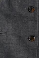 Blazer largo gris oscuro, de corte recto y largo, con escote redondo sin solapa y cierre frontal de botones oscuros. Presenta bolsillos ribeteados a la altura de la cadera y forro interior.