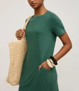 Vestido corto marrón oscuro, estilo camiseta, con escote redondo, mangas cortas y bolsillos laterales. El bajo es redondeado.