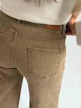 Jean de corte recto y tiro medio, en color camel con acabado desgastado. Presenta diseño clásico de cinco bolsillos, cierre frontal con botón y cremallera, y costuras reforzadas en el ruedo.