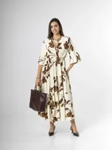 Vestido largo color crudo con estampado floral marrón, escote en V cruzado, mangas tres cuartos con volados y falda con niveles fruncidos.