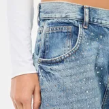 Jean de corte recto y tiro alto, color azul lavado, con detalle de strass aplicado en toda la parte frontal. Cuenta con cierre de botón y cremallera, y bolsillos laterales y traseros.