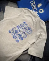 Remera oversize gris melange de manga corta, con estampa en la espalda de caracoles marinos en tonos azules y texto en rosa.