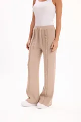Pantalón de tejido de punto color beige, de corte recto y holgado, con cintura elástica con cordón ajustable y detalle de costuras desflecadas verticales en el frente.