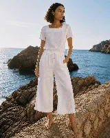 Pantalón capri de lino color blanco, con cintura elástica ajustable mediante cordón y detalles de flecos en los dobladillos.