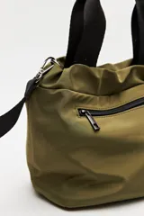 Cartera tipo bolso de nylon negro, con diseño utilitario y formato flexible que se ajusta con cordón en la parte superior. Posee asas de mano y una correa ajustable y desmontable para llevar cruzada. Incluye bolsillo frontal con cierre y herrajes metálicos.