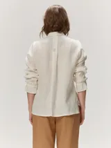 Camisa de lino liviano color tostado, con silueta relajada, cuello mao, alforzas verticales frontales, mangas con volumen y puños elastizados con volados.
