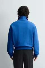 Sudadera de algodón azul con cuello alto y cierre frontal de cremallera de un cuarto. Presenta un corte regular y puños y bajo en rib.