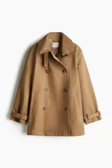 Gabardina corta de sarga color camel, con diseño holgado y doble botonadura. Presenta cuello convertible, bolsillos laterales ribeteados y trabillas ajustables con hebilla revestida en cuello y puños.