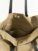 Bolso tipo tote de lona color beige con asas de cuero sintético negro, con hebilla decorativa. Tiene bolsillos laterales y es de gran capacidad.