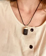 Collar con cordón de cuero negro y dije rectangular de piedra negra con detalles dorados.