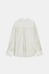 Camisa de mujer fluida de ZARA WOMAN COLLECTION, confeccionada en hilatura con mezcla de lyocell. Presenta escote en pico, manga larga con puños marcados y bajo asimétrico, con cierre frontal de botones ocultos.