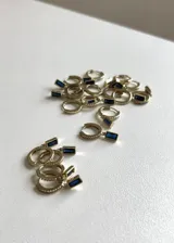Aros dorados tipo argolla con incrustaciones de circonitas y dije rectangular colgante con piedra azul.