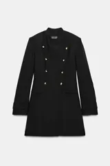 Vestido tipo blazer de corte estructurado, color negro, con cuello subido y cierre frontal cruzado con botones metálicos dorados. Presenta mangas largas con trabillas en los puños y bolsillos de vivo decorativos en el frente.