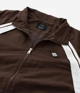 Campera deportiva de poliamida color marrón con detalles en blanco en los hombros y mangas. Presenta cierre frontal completo, cuello alto y puños elásticos.